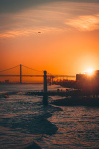 Silhouette bridge over sea against orange sky