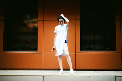 Full length of young woman standing on walkway against orange building