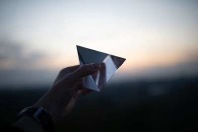 Midsection of person holding paper against sky during sunset