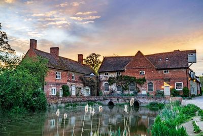 Houses by lake and buildings against sky during sunset