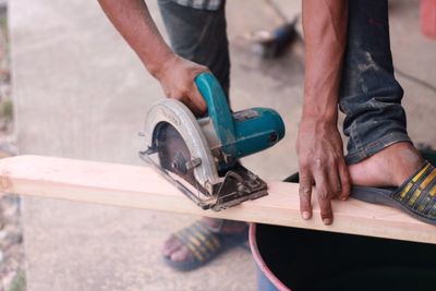 Low section of man cutting wood at workshop