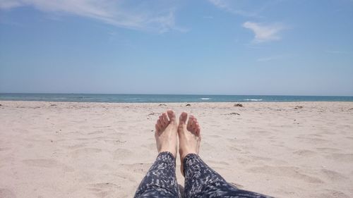 Low section of woman relaxing at beach against sky