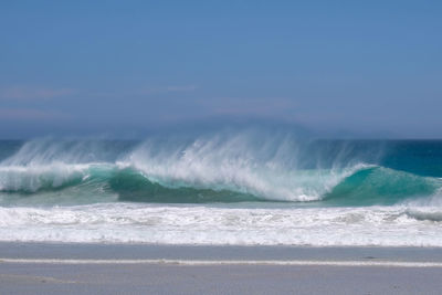 Waves splashing on shore against sky