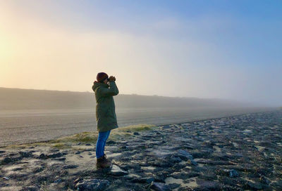 Side view of woman with binoculars standing on land