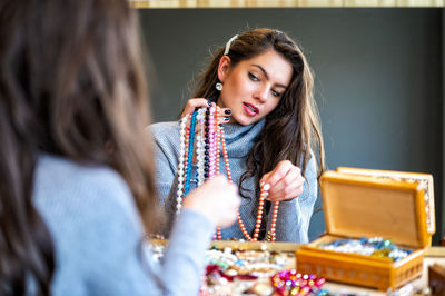 Reflection of a woman in mirror choosing and trying different jewelry, soft focus, close-up