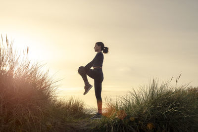 Silhoutte of a sporty woman doing a leg stretch exercise at sunrise.