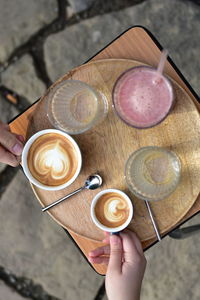 Cappuccino, macchiato, raspberry lemonade and two water glasses on a wooden tray, on a table