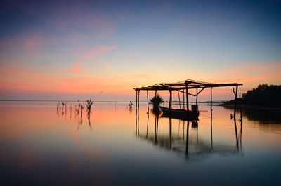 Silhouette wooden posts in lake against sky during sunset