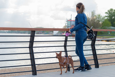 Young girl walking with her cute miniature pinscher by the lake.