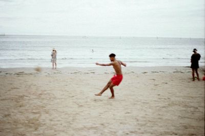 Full length of shirtless boy on beach against sky