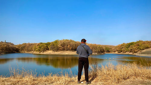 Rear view of man looking at lake against sky