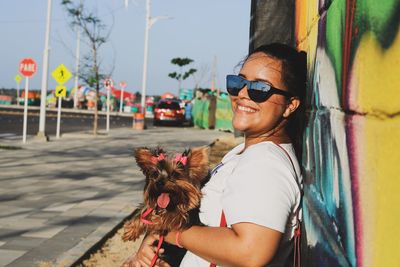 Smiling young woman with dog leaning on wall