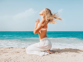 Side view of woman meditating on beach against sky