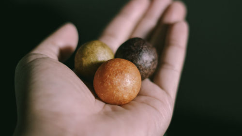 Close-up of hand holding apple against black background