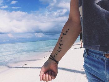 Tattooed birds on man hand at beach