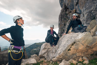 Concept: adventure. three of climbers with helmet and harness. a man and two women. resting relaxed sitting on a rock. via ferrata in the mountains.