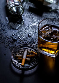 High angle view of whiskey glass and cigarettes in ashtray on table