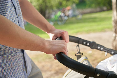 A young dad walking in the park with a baby in a stroller. close-up of men's hands. father's day