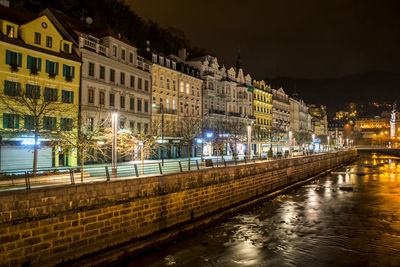 Illuminated buildings by river in city at night