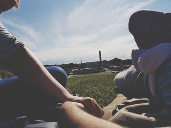 Low section of man sitting on field against sky