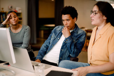 Thoughtful businessman looking at laptop while sitting with female colleagues in office