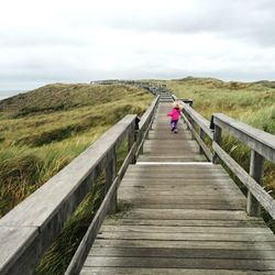 Wooden footbridge leading towards landscape against sky