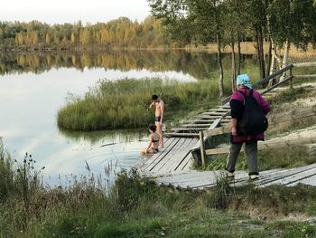 Heterosexual couple talking by lake while rear view of senior woman walking on wooden steps