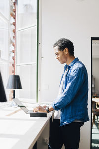 Side view of computer hacker working on laptop at desk by window in office