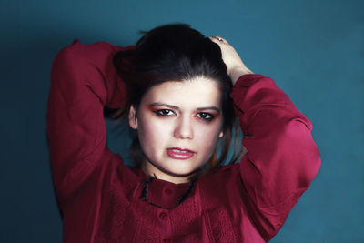 Portrait of beautiful woman with hand in hair standing against blue wall