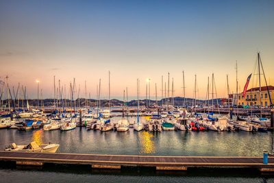 Sailboats moored in harbor at sunset