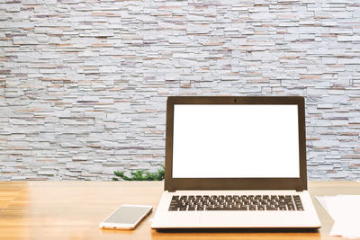 Laptop and mobile phone on table against wall