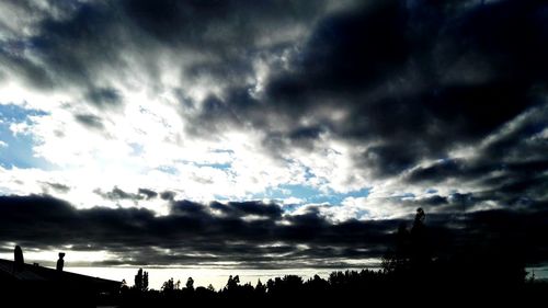 Low angle view of storm clouds over silhouette trees