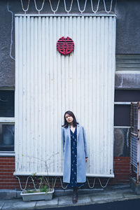 Full length portrait of woman standing against door