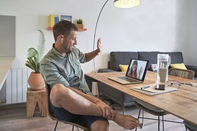 Smiling handsome businessman waving at female colleague through video call on laptop while working from home