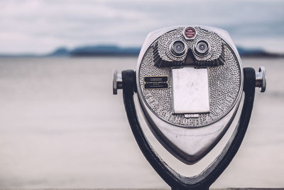 Close-up of coin-operated binoculars at beach against cloudy sky