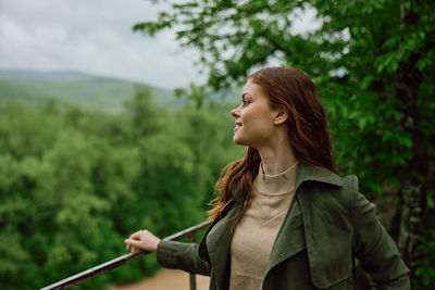 Smiling woman looking away by railing in forest
