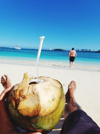 Close-up of man holding coconut drink  against clear blue sky