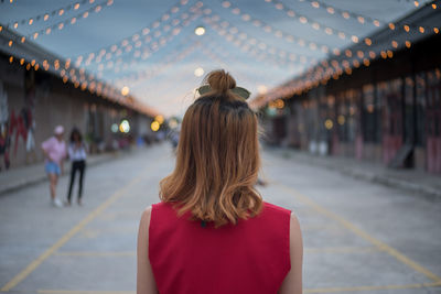 Rear view of woman walking on illuminated road