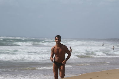 Shirtless young man running at beach against clear sky