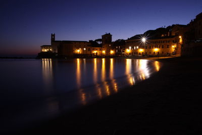 Illuminated historic building reflecting in sea against sky