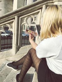 Rear view of woman photographing while sitting on window