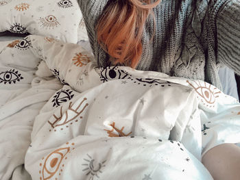 Midsection of woman sitting on bed at home