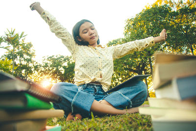 Happy young woman sitting on plant against trees