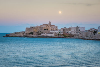 Buildings by sea against sky during sunset