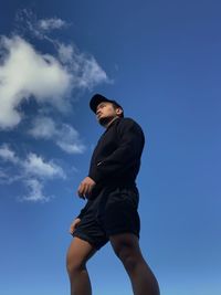 Low angle view of young man against blue sky