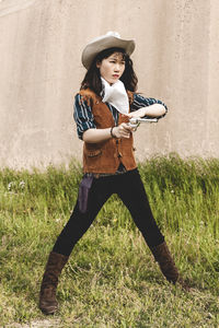 Young woman aiming gun while standing against wall