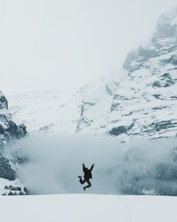 Man jumping in snow against sky