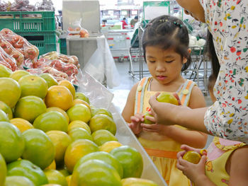 Midsection of mother giving oranges to daughters at market