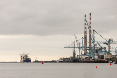 Cranes at commercial dock against sky