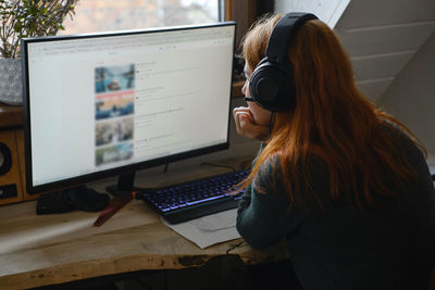 Middle age woman listening to music in big headphones near computer at home. creating play list